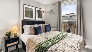 Une chambre bien rangée, avec un lit, une table de chevet, une lampe et une œuvre d’art encadrée accrochée au mur.