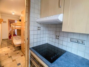 A compact kitchen with a black stove, white tiled walls, and a wooden door leading to a bedroom. - 100m from resort center, 3rd floor, balcony, tv, ski locker, 39m², Tignes (Tignes)