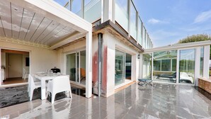 A modern house with a patio area featuring a dining table and chairs, large glass doors, and a wet floor. - Heated indoor swimming pool - oyster beds (Le Tour-du-Parc)