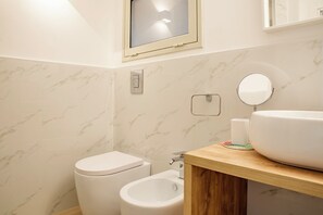 A bathroom with a toilet, bidet, sink, and mirror. - Helios Duplex a due passi da Ortigia by Wonderful Italy (Syracuse)