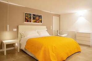 A modern bedroom with a large bed, a bedside table, a chair, and two paintings on the wall. - Helios Duplex a due passi da Ortigia by Wonderful Italy (Syracuse)