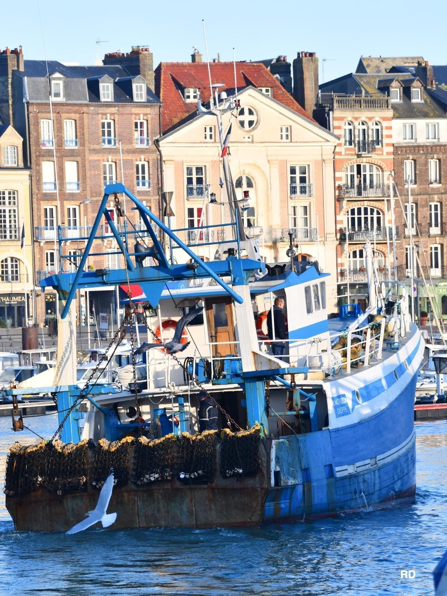 Un bateau de pêche bleu était amarré dans un port, avec des bâtiments en arrière-plan.