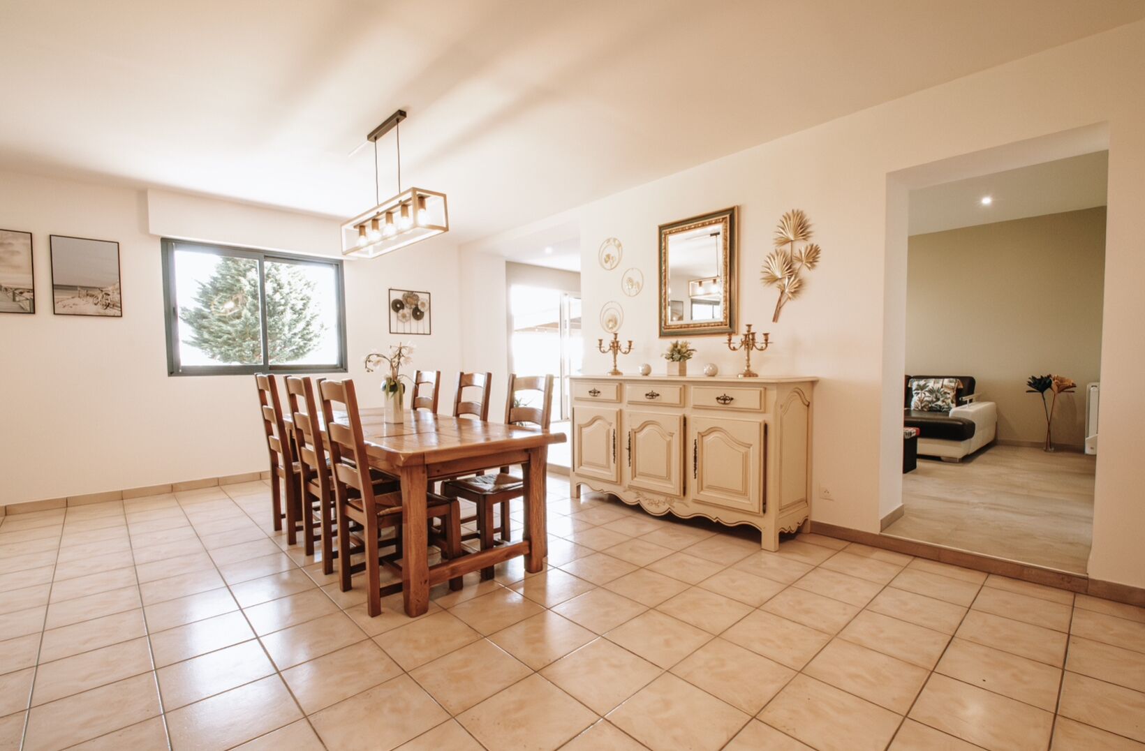 A spacious dining area with a wooden table and chairs, a cream-colored cabinet, and a large window providing natural light.