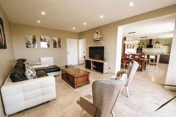 A living room with a sofa, a coffee table, and a TV. There is a dining area with a table and chairs.