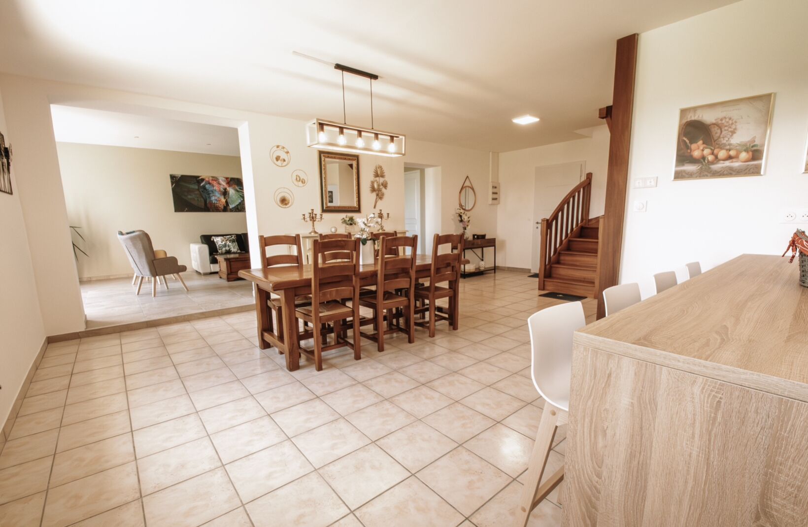 A spacious dining area with a wooden table and chairs, a chandelier, and a staircase leading to another level.