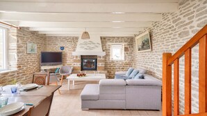 A cozy living room with a stone wall, a fireplace, a television, and a wooden staircase. - House for 7 300m from the beach - Guilvinec (Le Guilvinec)
