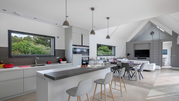 A modern kitchen with a large island, bar stools, and a dining area with a white sofa and table.