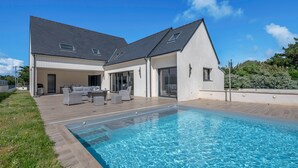 A modern house with a swimming pool, outdoor seating, and a large patio area.