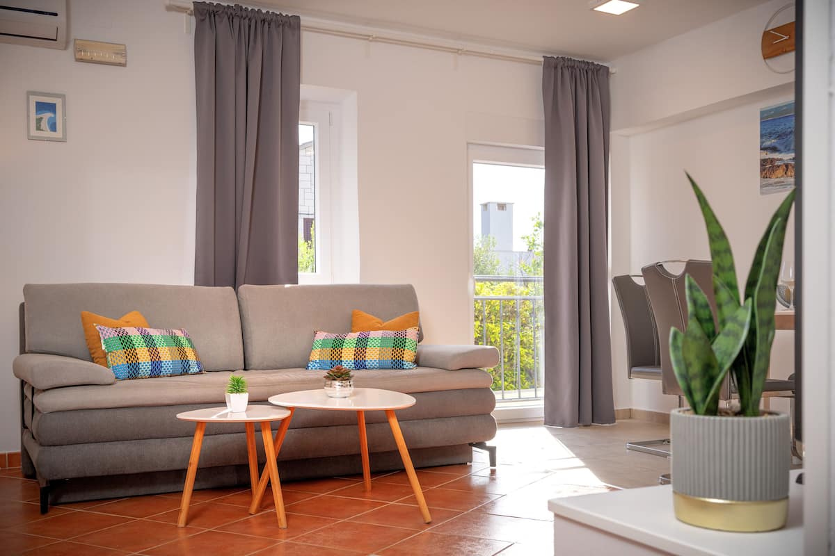A living room with a grey sofa, two small round tables, and a potted plant.