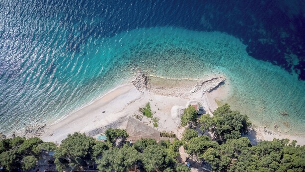 An aerial view of a coastal area with a beach, rocky shoreline, and dense greenery. - Beachfront Villa near Zlatni rat (Bol)