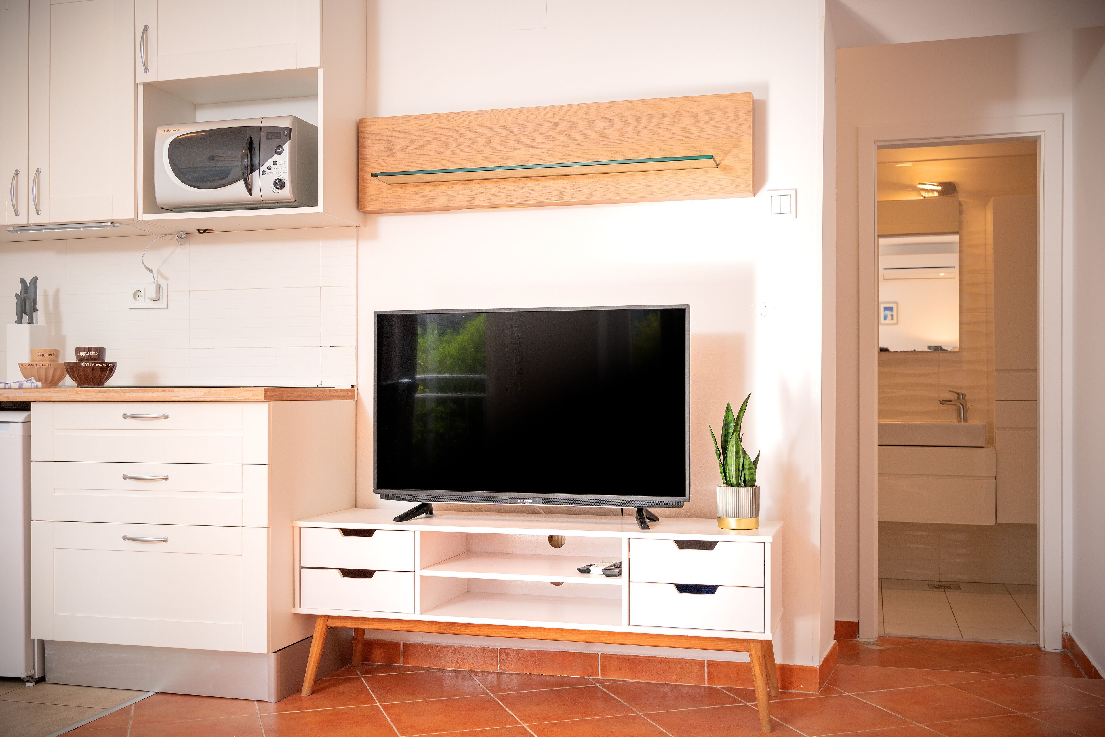 Una cucina moderna con forno a microonde integrato, TV a schermo piatto su un supporto in legno e una piccola pianta in vaso.