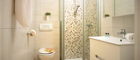 Un bany modern amb dutxa amb envàs de vidre, vàter i un lavabo amb mirall a la part superior.