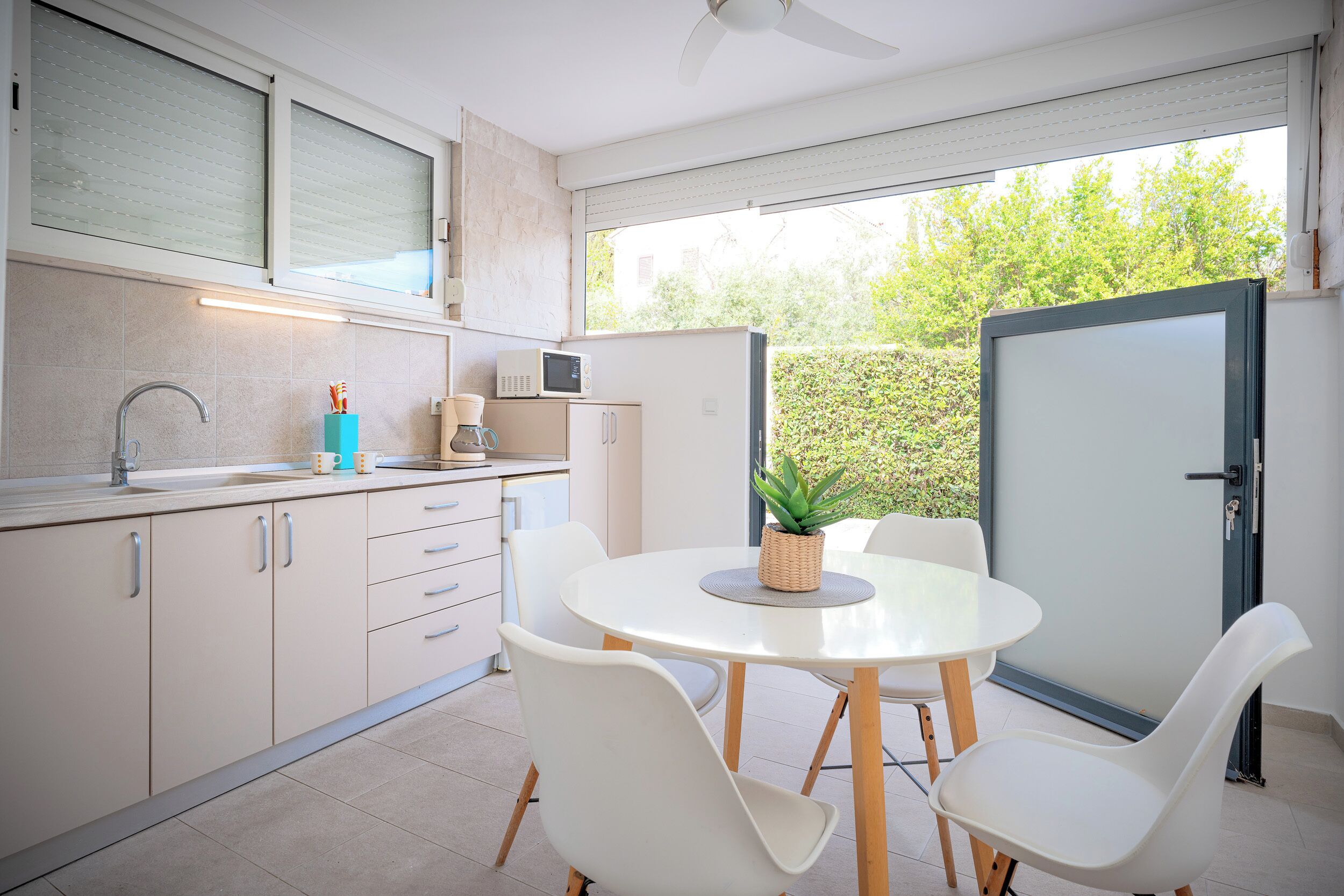 Eine moderne Küche mit Essbereich, weißen Schränken, einer Mikrowelle und einem Blumentopf auf dem Tisch.