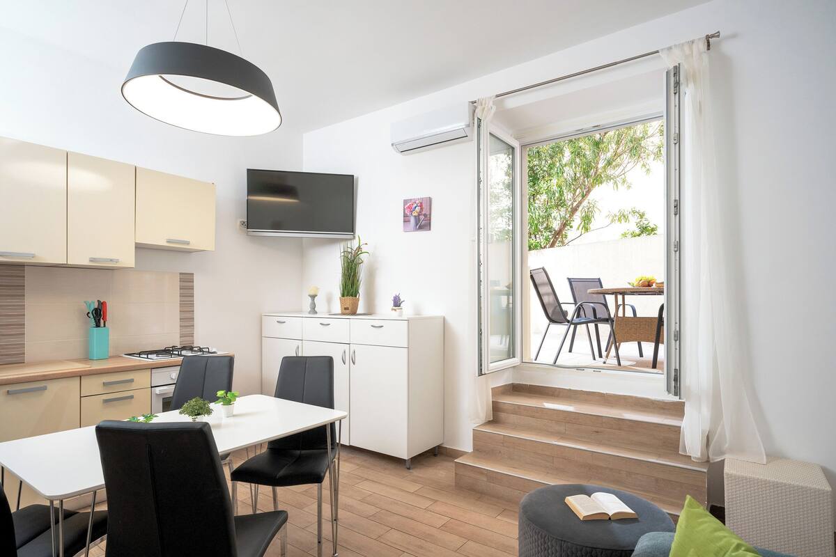 A modern kitchen with white cabinets, a flat-screen TV, and a dining area with a table and chairs.