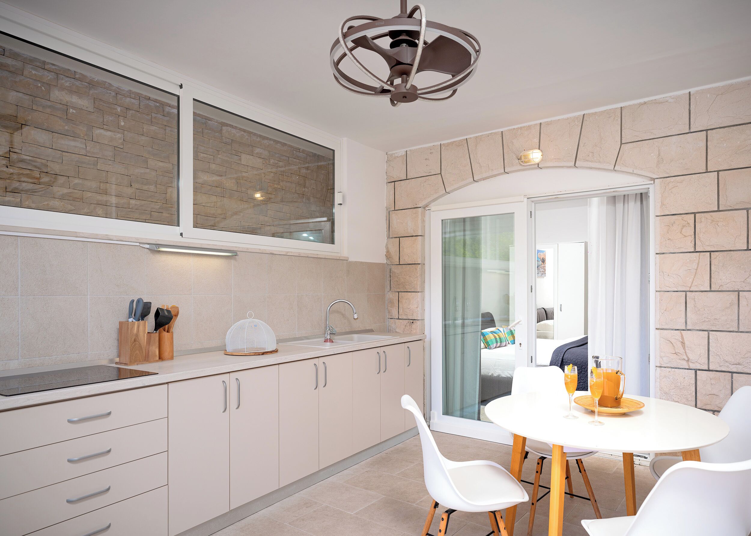 A modern kitchen with a stone backsplash, a built-in oven, and a dining area with a table and chairs.