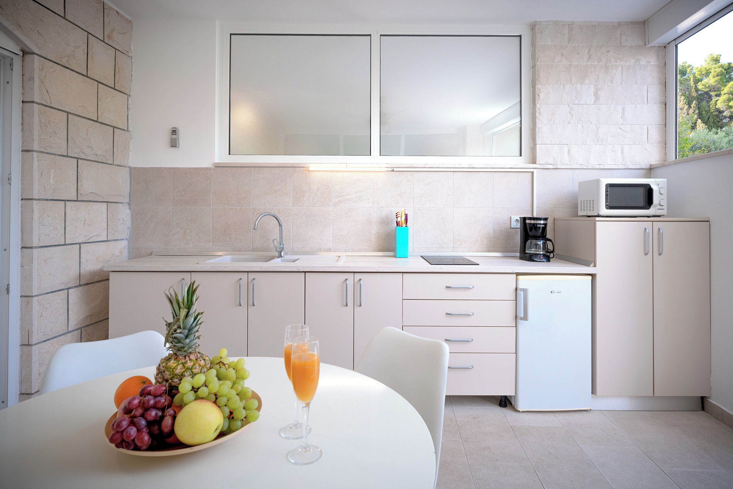Una cucina moderna con mobili bianchi, un forno a microonde integrato e un piccolo frigorifero.