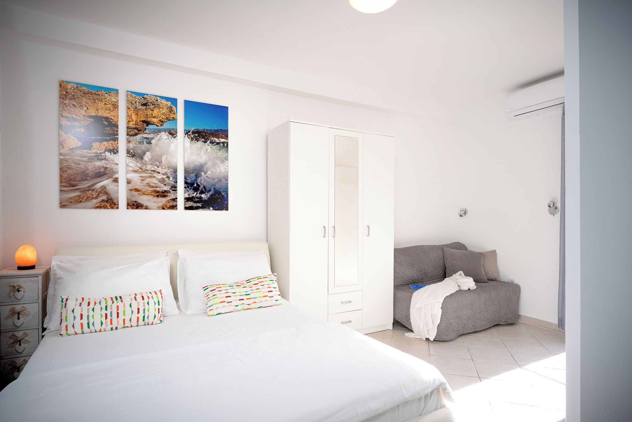 Een slaapkamer met een bed, een kledingkast, een nachtkastje met een lamp en een bank.