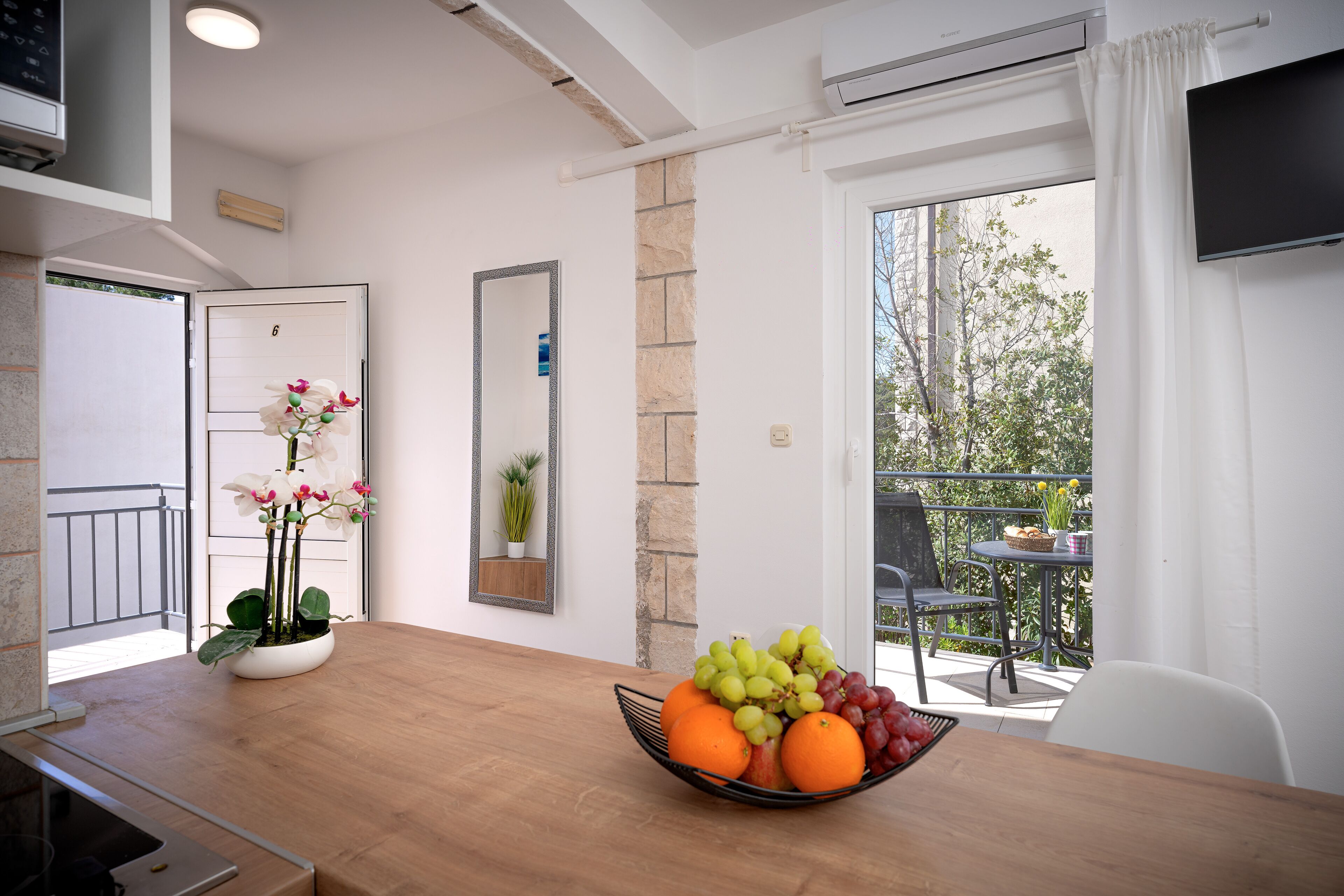 A modern kitchen with a wooden countertop, a fruit bowl, a potted orchid, and a view of the outdoor balcony.