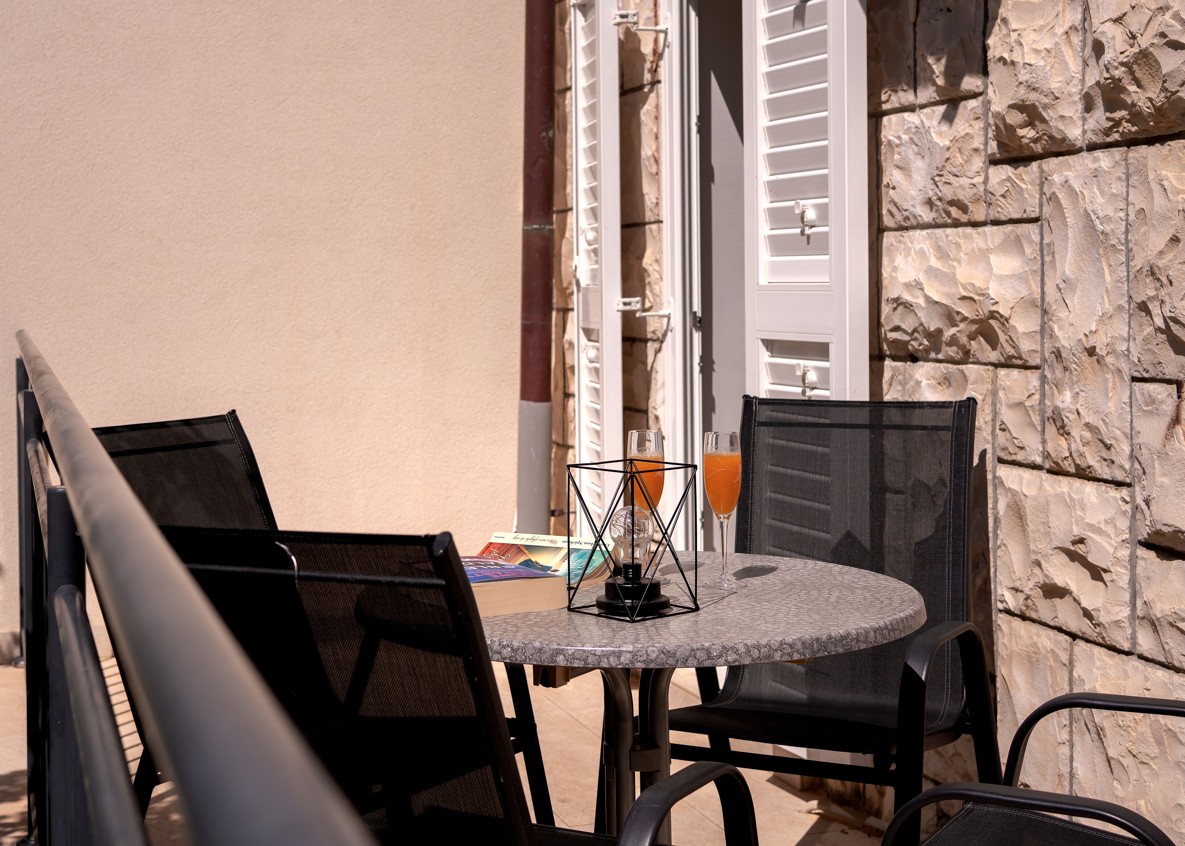 A small outdoor seating area with a round table and two chairs, a book, and a glass of orange juice.