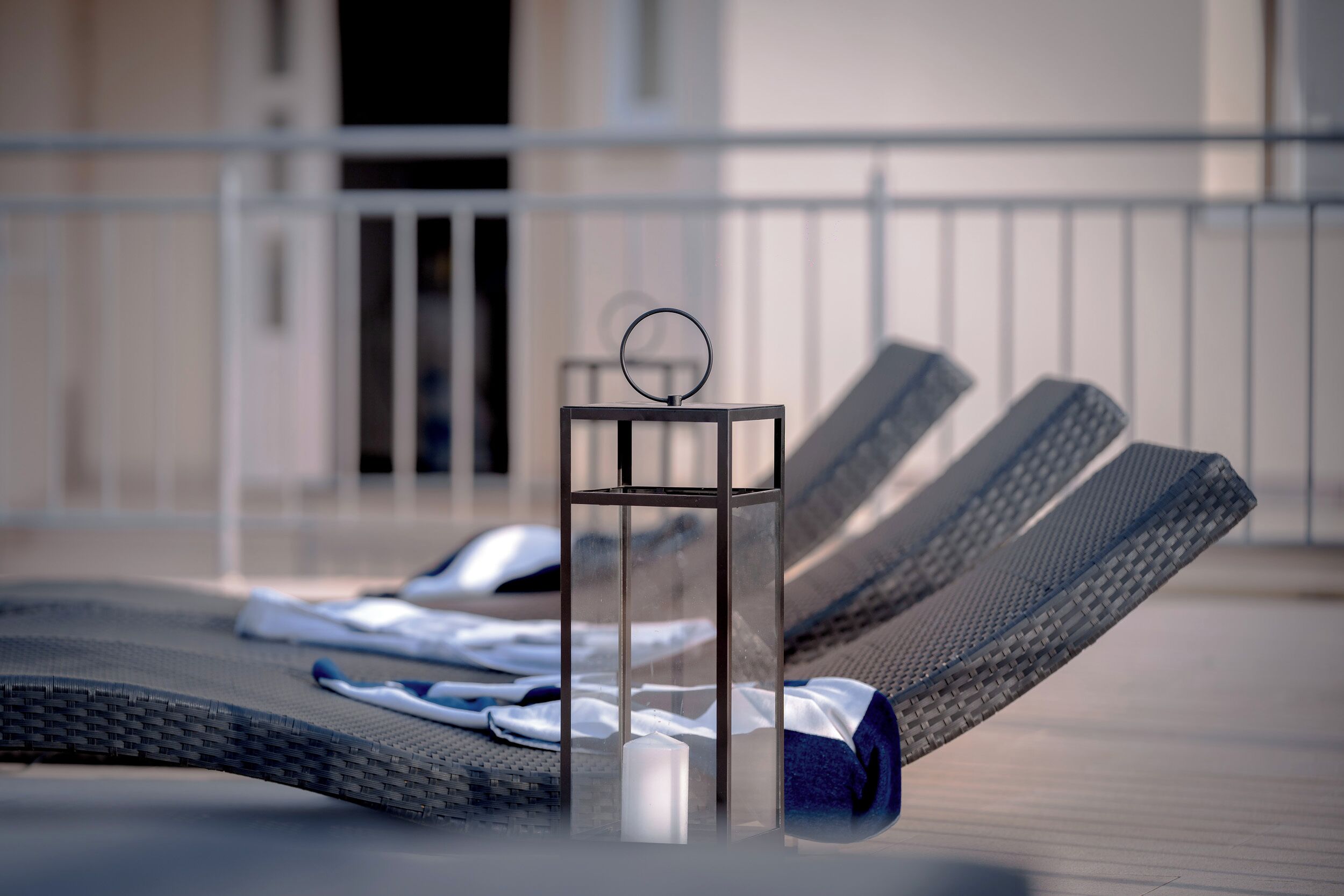 A sun lounger with a towel and a candle, and a glass table with a ring on top.