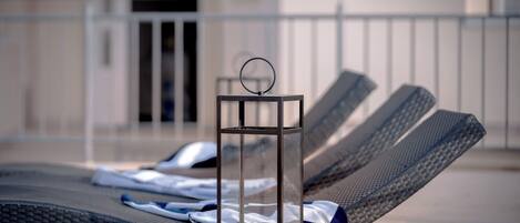 A sun lounger with a towel and a candle, and a glass table with a ring on top.
