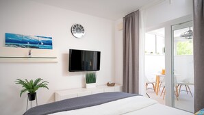 A modern hotel room with a bed, a flat-screen TV, a painting, a clock, and a view of the outdoors. - Beachfront Villa near Zlatni rat (Bol)