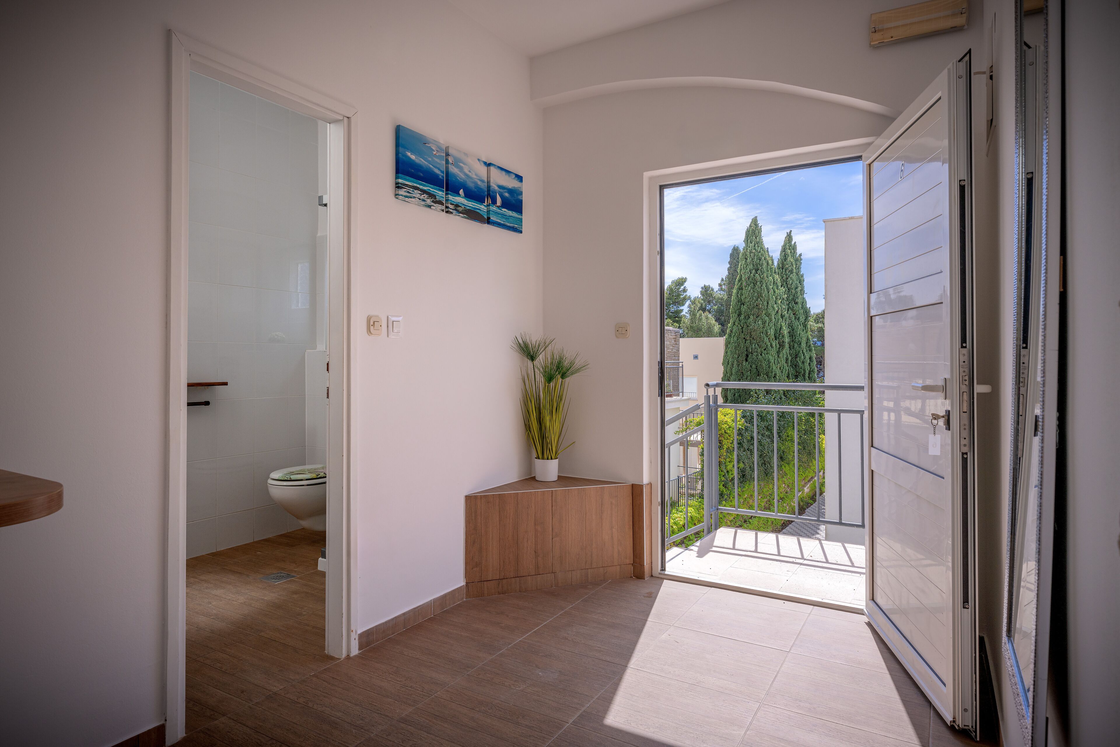 Un baño moderno con inodoro, una planta en maceta y un cuadro en la pared.