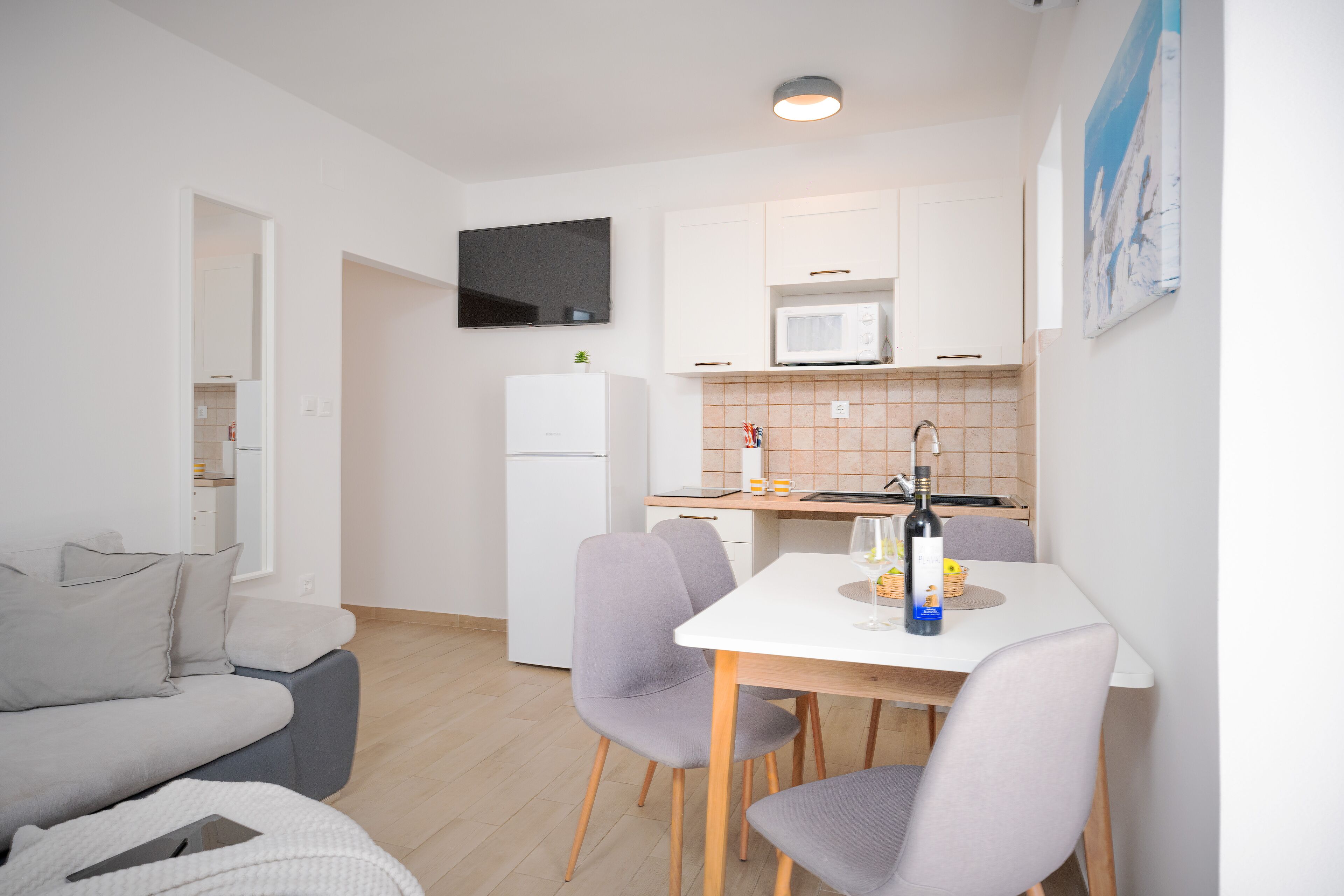 Un espacio habitable compacto con kitchenette, un televisor de pantalla plana sobre el microondas y una zona de comedor con mesa y sillas.