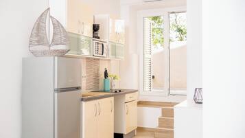 Una cocina moderna con armarios blancos, un microondas integrado y un refrigerador. Hay una ventana con persianas, un fregadero y un jarrón con flores en la encimera.