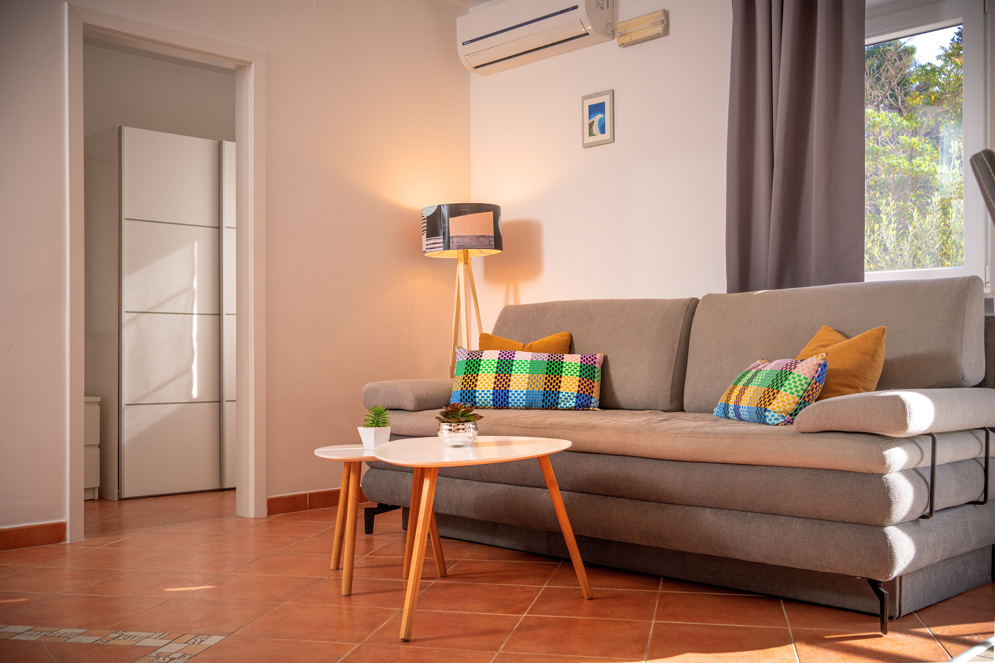 A living room with a sofa, a small table, a floor lamp, and a window with curtains.