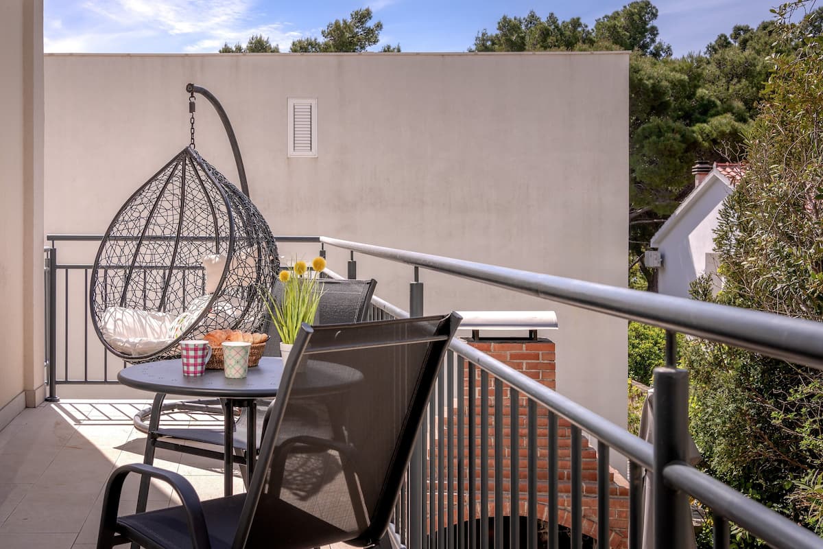 A balcony with a hanging chair, a table with a basket of bread, a mug, and a bottle of water.