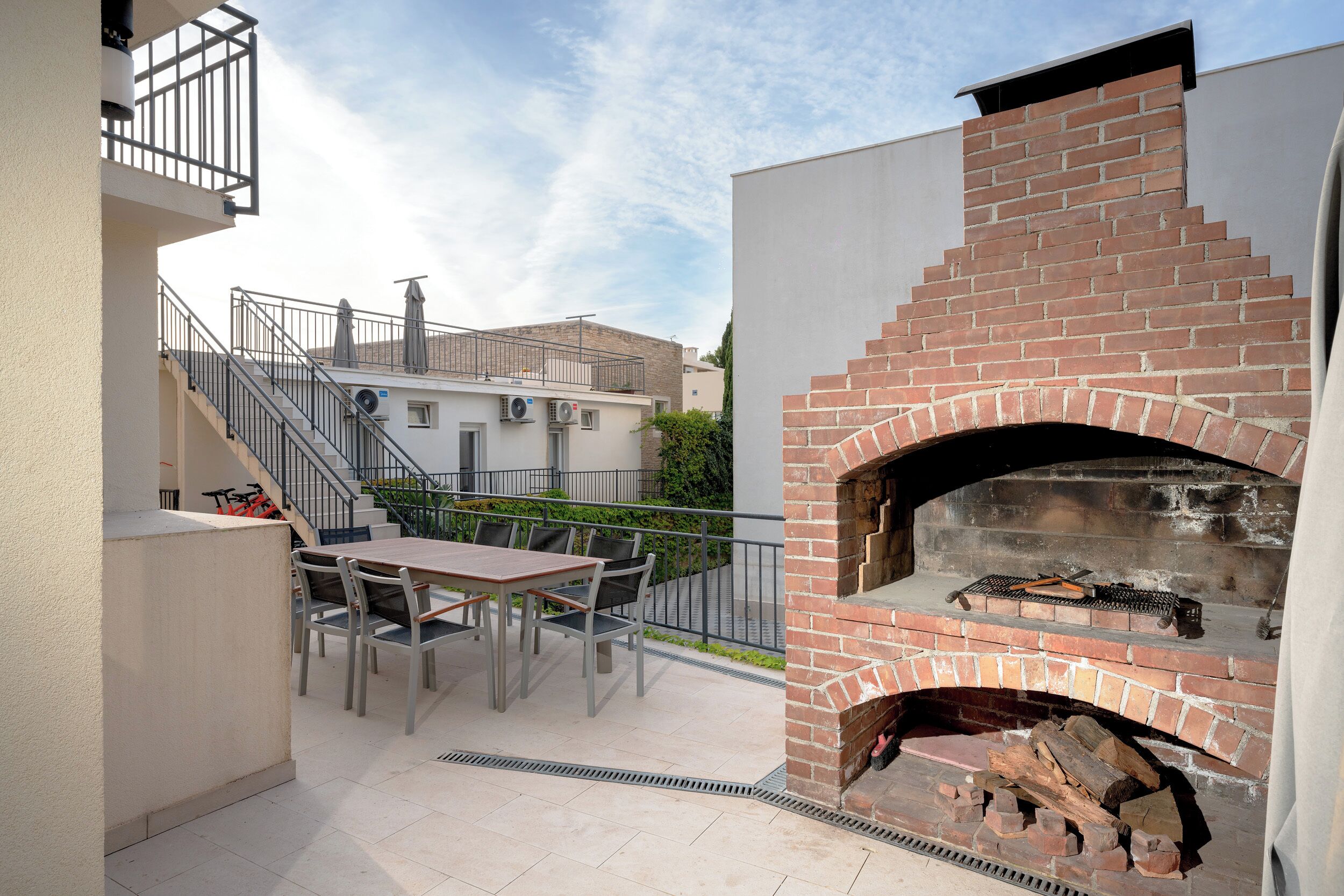An outdoor patio with a brick oven, a table with chairs, and a staircase leading to an upper level.