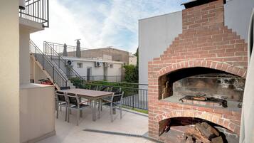 An outdoor patio with a brick oven, a table with chairs, and a staircase leading to an upper level.
