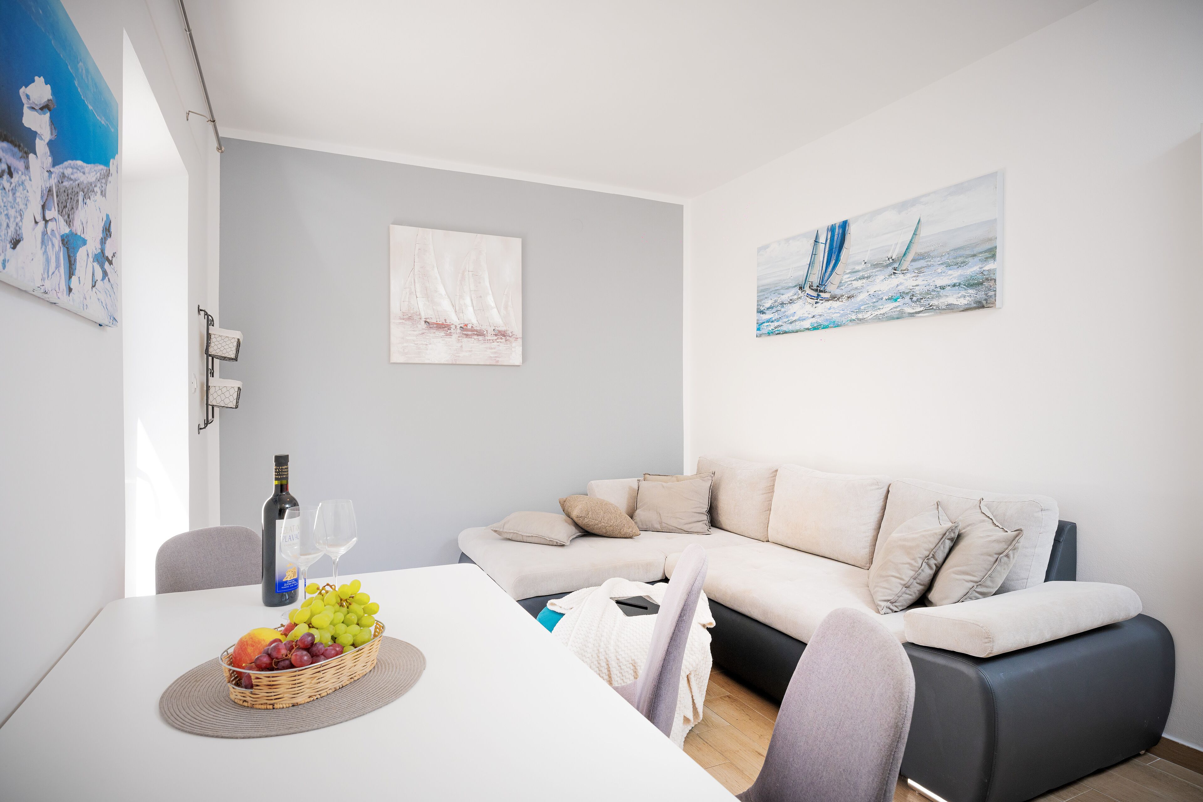 A modern living room with a sofa, a dining table with fruit and wine, and artwork on the walls.