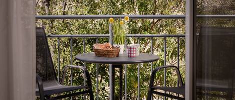 A balcony with a round table, two chairs, a wicker basket, a checkered cup, and a vase with yellow flowers.