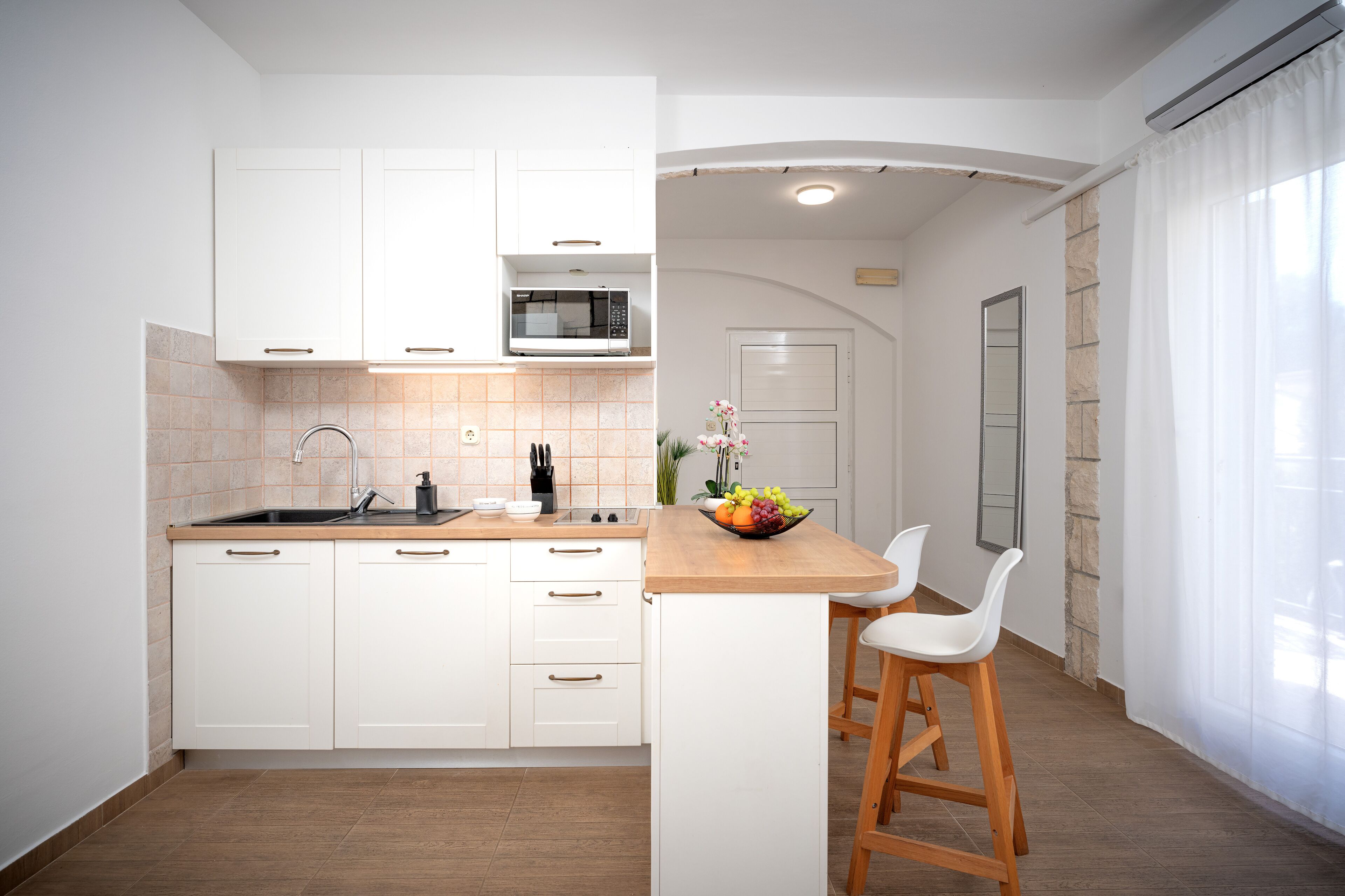 Una cocina moderna con gabinetes blancos, un microondas y una isla de madera con taburetes.
