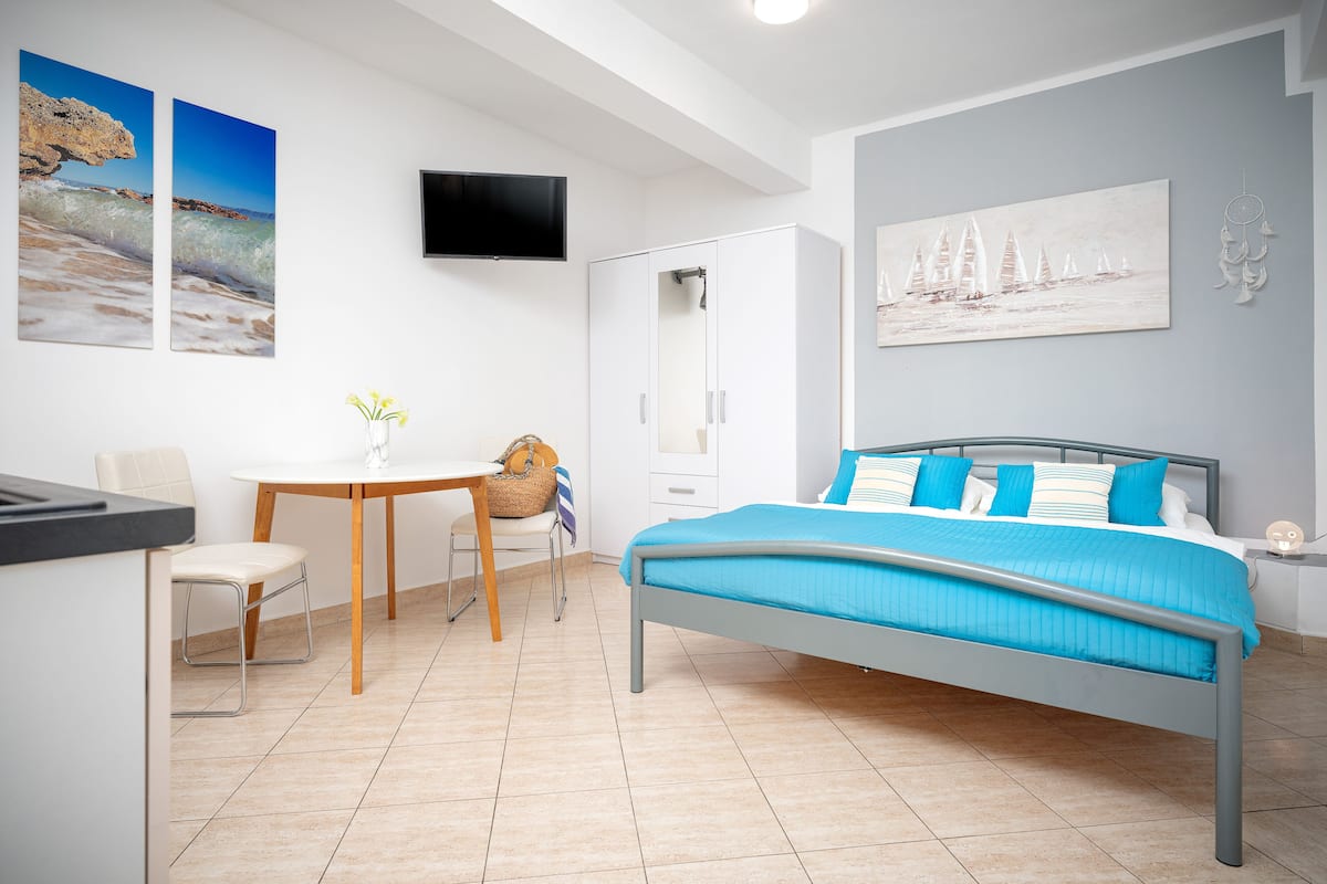 A bedroom with a bed, a desk, a chair, a wardrobe, and artwork on the walls.
