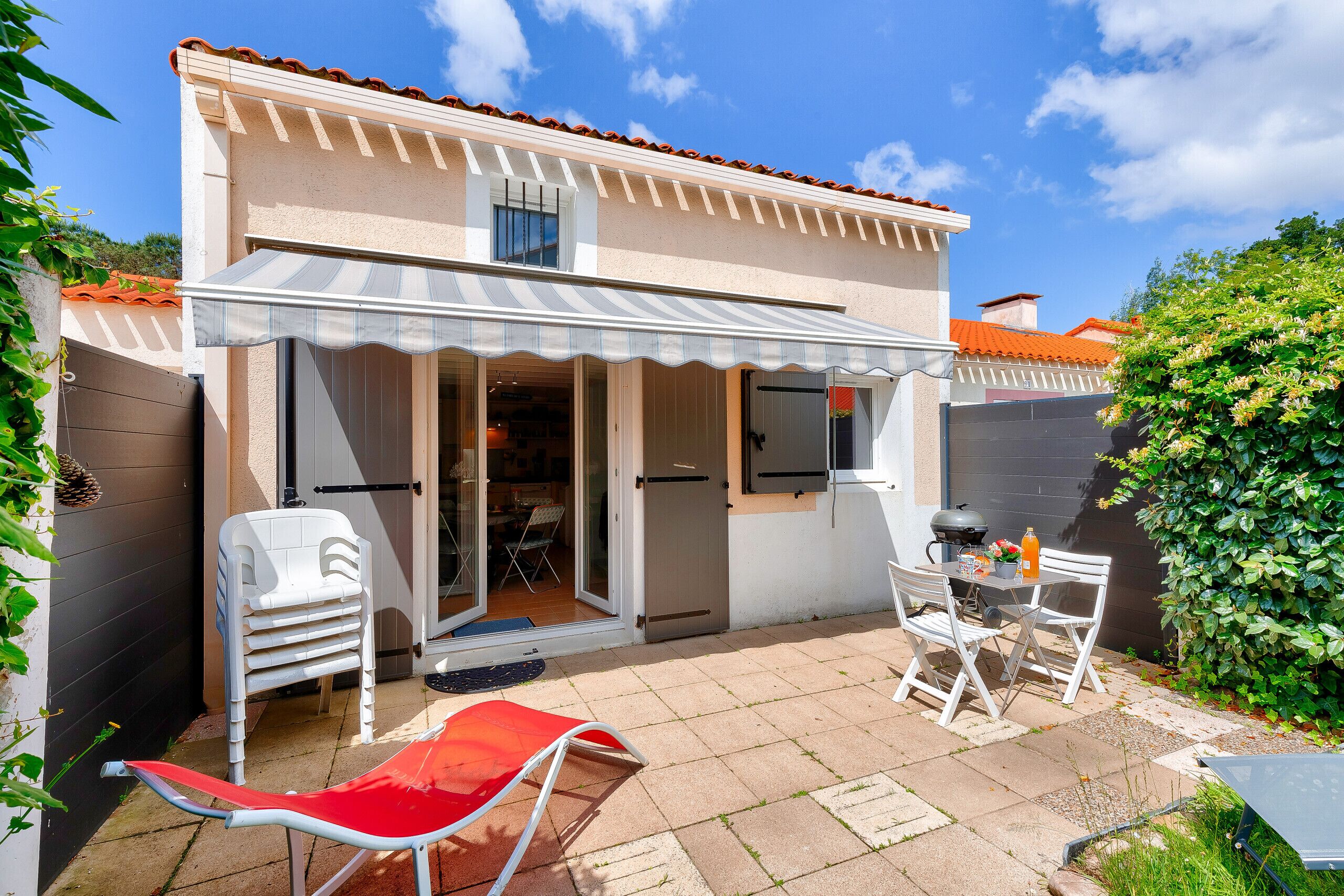 Une maison dotée d’un patio couvert, d’un espace barbecue et d’un ensemble de mobilier de jardin pour les repas.