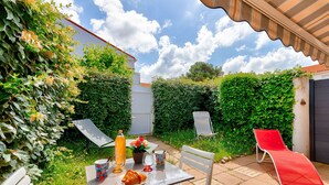 A patio with a table set for two, a red lounge chair, and a white chair.
