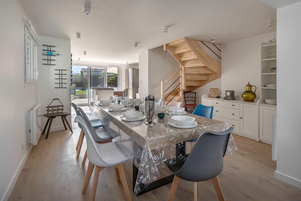 A modern kitchen with a wooden staircase, a dining area with a table set for four, and a view of the outdoors.