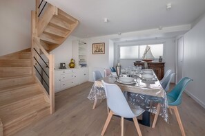 Enjoy meals in this spacious dining area with a long table for four, surrounded by matching chairs and a large window offering a view of the outdoors.