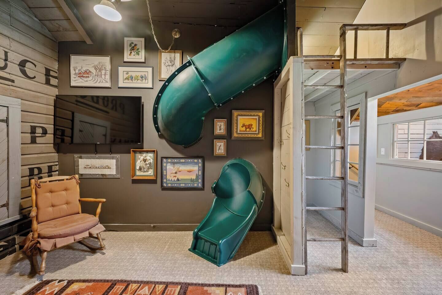 A room with a large green slide, a wooden chair, and various framed pictures on the wall.