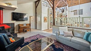 A spacious living room with a piano, a sofa, a television, and a large window overlooking a balcony.