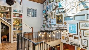 A spacious interior with a wooden staircase, a gallery wall with framed pictures, and a ceiling with skylights.