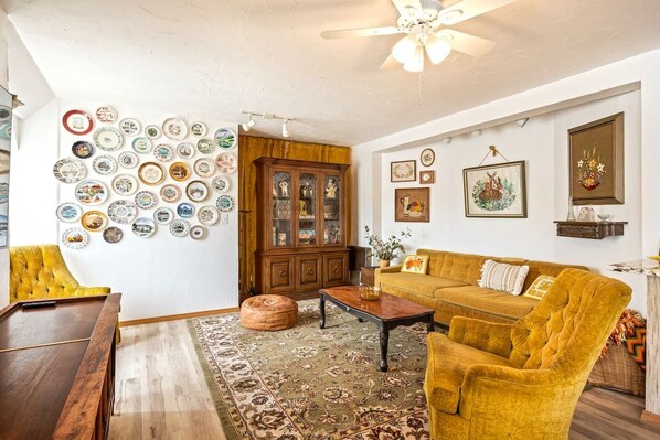 A living room with a yellow sofa, wooden cabinet, and a wall decorated with plates.