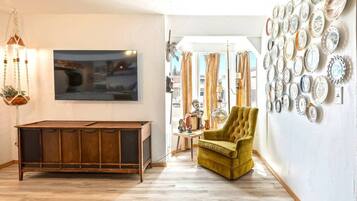 A living room with a wooden entertainment center, a television, a green armchair, and a wall decorated with bottle caps.