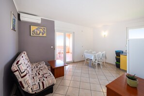 A living room with a sofa, a small table, a dining area with chairs, and a kitchen area with cabinets. - Comfortable Apartments Malina B4 br 4 (Novalja)