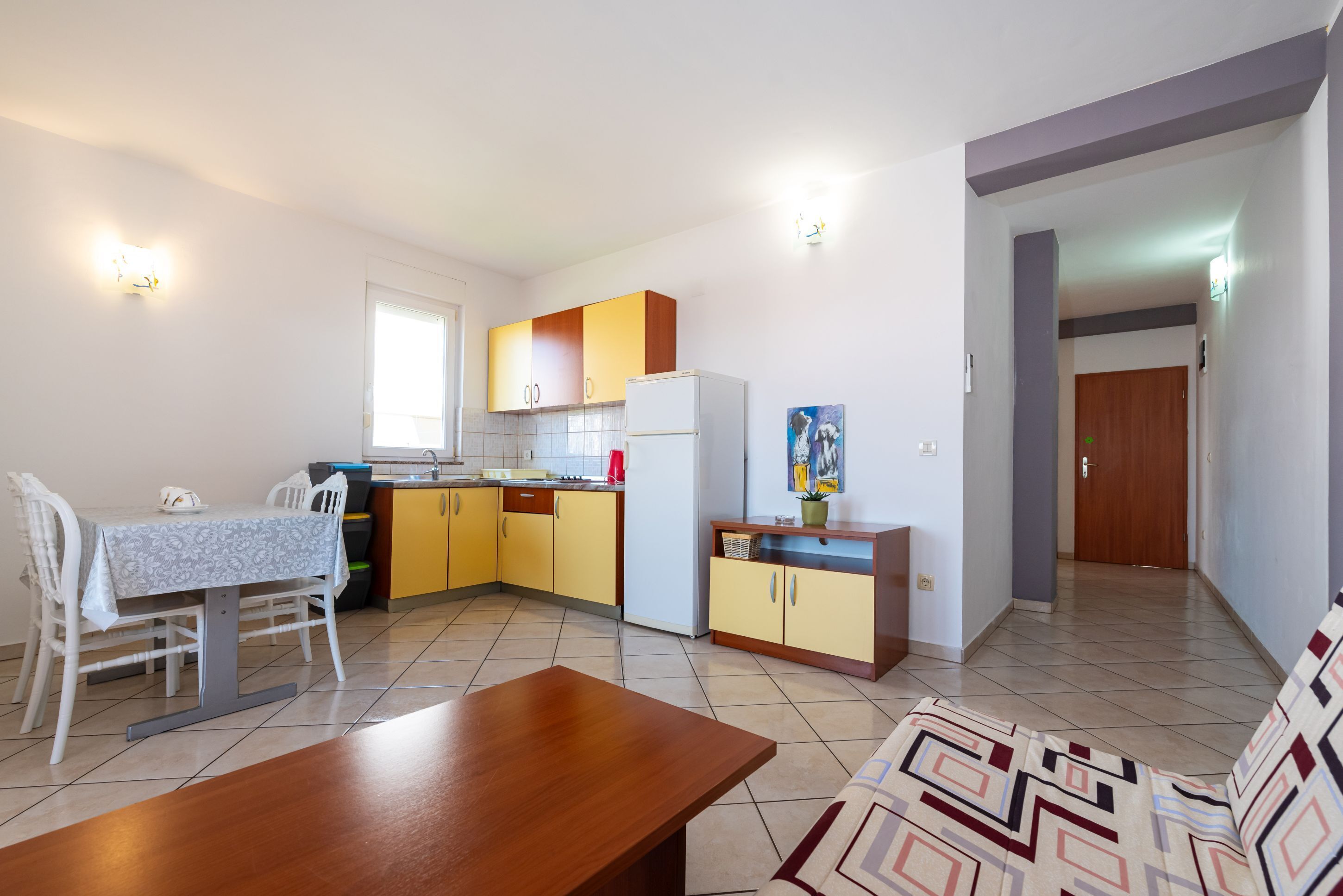 A compact kitchen with a dining table, a sofa, and a refrigerator.