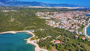 Vue aérienne d’une ville côtière avec une plage, un quartier résidentiel dense et un paysage montagneux en arrière-plan.