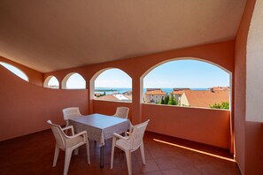 A balcony with a table and chairs, large arched windows, and a view of buildings and the sea. - Comfortable Apartments Malina B4 br 4 (Novalja)